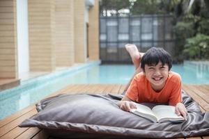 Retrato de niño feliz leyendo un libro acostado en la almohada de la cama, concepto de lectura educativa foto