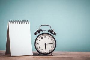 black retro alarm clock and blank note paper for text on wooden table with vintage style photo