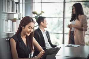 mujer de negocios que usa una tableta digital moderna mientras un compañero de trabajo interactúa en segundo plano en la oficina, reunión de trabajo en equipo y concepto de asociación. foto