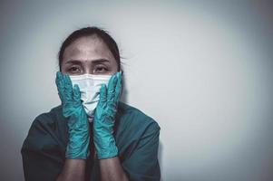 una enfermera asiática cansada y deprimida usa una máscara facial uniforme azul sentada en el piso del hospital, una joven doctora estresada por el trabajo duro foto