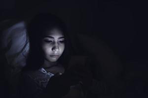 mujer asiática juega al teléfono inteligente en la cama por la noche, gente de tailandia foto