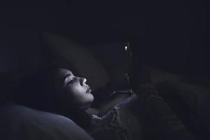 mujer asiática juega al teléfono inteligente en la cama por la noche, gente de tailandia foto