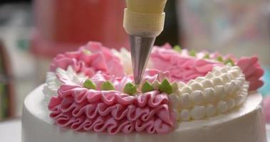 Close-up top view The chef is squeezing the white cream into a garland on top of the cake. video