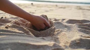 hand tar sand från de strand i långsam rörelse. kvinna häller sand löpning genom fingrar långsam rörelse på de strand med Sol lysa skarpt och blå himmel. video