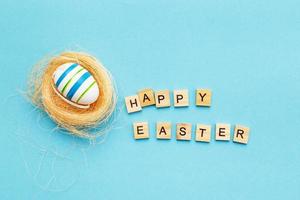 inscription happy easter with colorful handmade painted egg in the nest on blue background photo