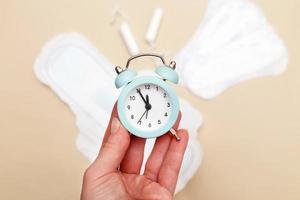 Women's hygiene pads with tampons and alarm clock on beige background photo