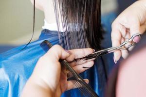 haircuting in a beauty professional salon. hairdresser's hands cutting brunette hair close photo
