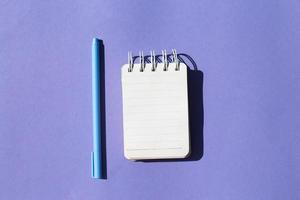 Top view of blank note paper with pen on purple background photo