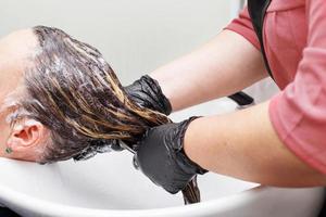 The hairdresser in black gloves washing brunette woman's hair in the beauty salon. photo