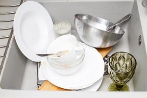 Pile of dirty dishes like plates, cutlery in the grey modern granite sink in the kitchen photo