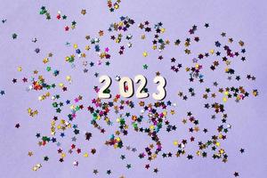 inscription 2023 with wooden numbers on purple background with multicolored confetti.Festive concept photo