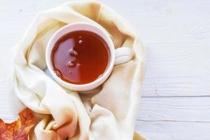 hojas de otoño con una taza de té o café junto a una bufanda sobre un fondo de madera con espacio para copiar foto