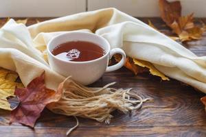 autumn leaves with a cup of tea or coffee next to a scarf on a wooden background with copy space photo