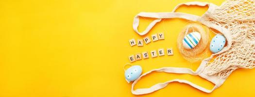 inscription happy easter with colorful painted eggs and cotton string bag on orange background photo