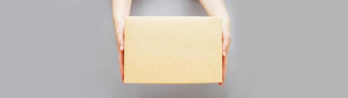 manos humanas sosteniendo entrega caja de cartón sobre fondo gris. concepto de entrega y compras en línea. foto