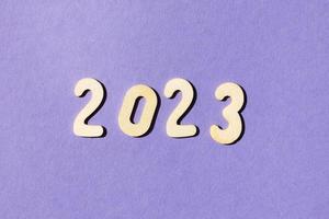 inscription 2023 with wooden numbers on purple background .Festive concept photo