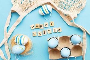 inscription happy easter with colorful painted eggs and cotton string bag on blue background photo