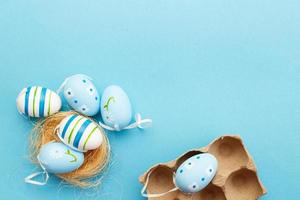colorful handmade painted eggs in the nest and cardboard box on blue background photo
