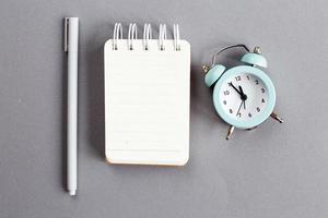 Top view of blank note paper with pen and alarm clock on gray background photo