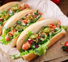 perrito caliente con pimientos jalapeños, tomate, pepino y lechuga sobre fondo de madera foto