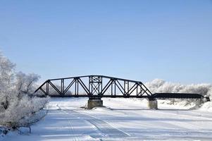 a railway bridge over a frozen river with frost covered trees on the shore