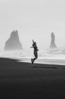 turista feliz saltando sobre la fotografía escénica de la playa monocromática del norte negro foto