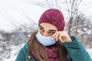 Avoid touching your eyes. Woman wearing face mask rubbing her eye outdoor. Young woman touching her eye with dirty hand. Don't touch your face, stop spreading Coronavirus photo