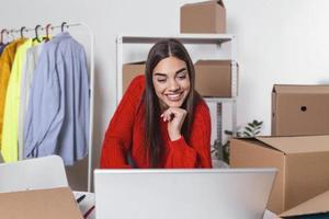 Woman packing item that she sells online. Working woman at online shop. She wearing casual clothing and checking on laptop address of customer and package information. small owner business photo