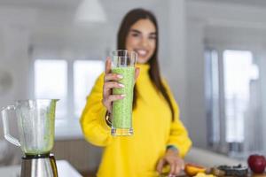 Young woman holding glass of smoothie. Beautiful smiling woman shoeing energetic drink full of vitamins. Raw food diet, vegetarian nutrition, organic detox meal photo