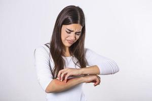 Young woman scratching her arm due to itching on a gray background. Female has an itching arm. The concept of allergy symptoms and healthcare