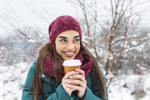Happy young woman with disposable cup of coffee or tea wearing warm clothing. Beautiful girl holding disposable cup,standing outdoor on winter photo