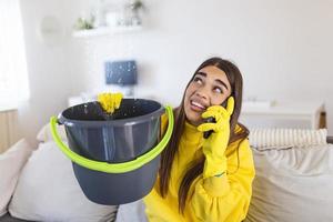 mujer sorprendida llamando a un plomero mientras recolectaba agua que se escapaba del techo usando un utensilio foto