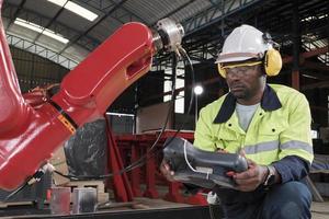 An African American production engineer test and control robotic arm in mechanical manufacturing factory, intelligent automatic machines in industrial business, and futuristic technology innovation. photo