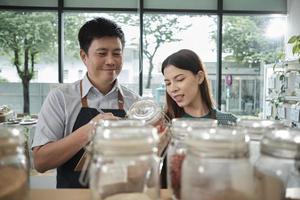 Two shopkeeper colleagues check stock of natural organic products in reusable containers shelves at refill store, zero waste, plastic-free grocery shop, and eco-friendly, sustainable lifestyles. photo