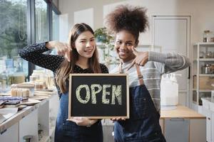 dos jóvenes comerciantes muestran un letrero abierto con sonrisas alegres en la tienda de recarga, trabajo feliz con productos orgánicos, comestibles sin desperdicio, mercadería ecológica y negocios sostenibles. foto