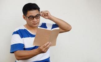 un hombre asiático de mediana edad usa anteojos y está leyendo un libro. concepto, problema de la vista. optometría. anteojos con lentes convexas o cóncavas. miopía.enfermedad ocular