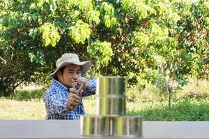 Asian man holds slingshot to play  shooting game, aim to shoot the  cans in forest. Concept, recreation activity, Hand-powered projectile weapon. Check the accuracy of target shooting. Fun game. photo