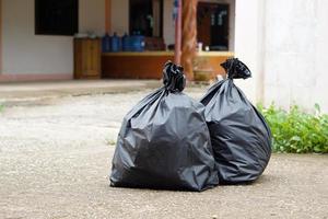 dos bolsas de plástico negras que contienen basura dentro frente a la casa. esperando a que los basureros se los lleven. concepto de gestión de residuos. recogidos para su eliminación. foto