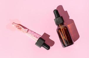 Flat lay of a pipette with pouring liquid and amber bottle on pink background. Copy space photo