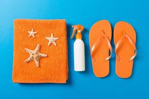 Top view of Beach flat lay accessories. sunscreen bottle with seashells, starfish, towel and flip-flop on Colored background with copy space photo