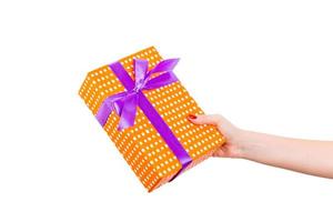 Woman hands give wrapped Christmas or other holiday handmade present in orange paper with purple ribbon. Isolated on white background, top view. thanksgiving Gift box concept photo