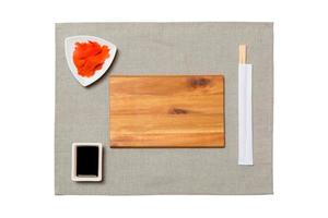 Empty rectangular brown wooden plate with chopsticks for sushi, ginger and soy sauce on grey napkin background. Top view with copy space for you design photo