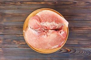 fresh large piece of pork on a round wooden cutting board. Top view on wooden background photo