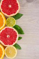 jugosas frutas cítricas cortan hojas de menta de fondo. naranjas, limones, limas, pomelos, hojas de menta sobre un fondo de madera brillante foto