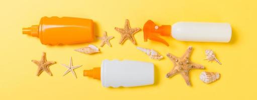 Sunscreen bottles with seashells on yellow table top view photo