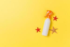 sunscreen cream with starfish and seashells in bottles on yellow background, top view photo