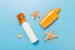 sunscreen cream with starfish and seashells in bottles on blue background, top view photo