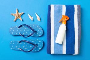 Top view of Beach flat lay accessories. sunscreen bottle with seashells, starfish, towel and flip-flop on Colored background with copy space photo