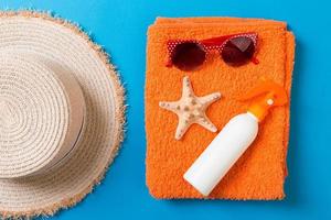 Summer beach flat lay accessories. Sunscreen bottle cream, towel and seashells on colored Background. Travel holiday concept with copy space photo