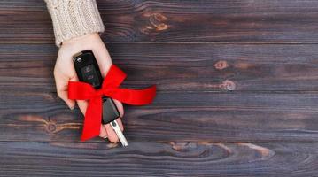 Woman hand hold car key with red bow. Giving a car as a gift Banner photo